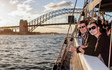 Couple on a tall ship enjoying Sydney Harbour views with Sydney Harbour Bridge in the background.