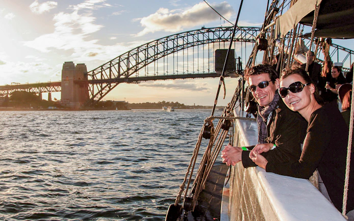 Couple on a tall ship enjoying Sydney Harbour views with Sydney Harbour Bridge in the background.