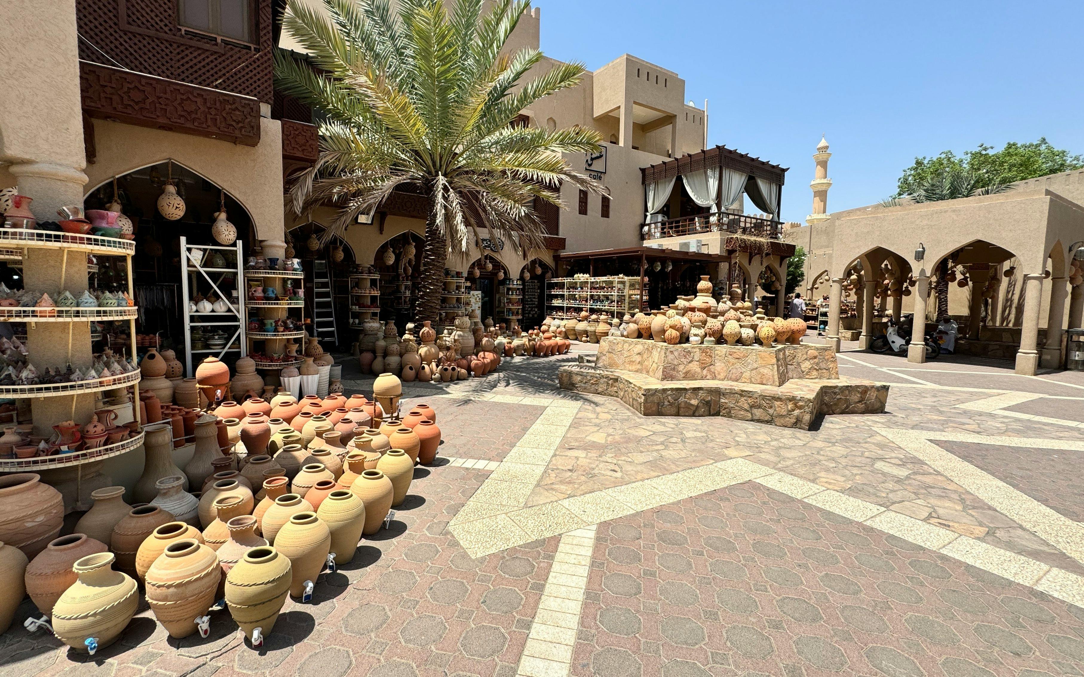 Pottery display at Nizwa Souq, Oman, with traditional clay pots and palm tree.