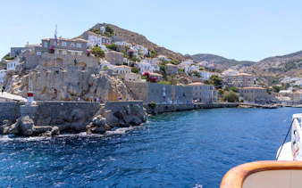 Hydra Island coastline with stone buildings and clear blue sea during Athens day cruise.