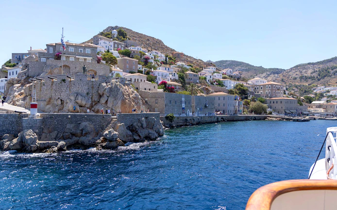 Hydra Island coastline with stone buildings and clear blue sea during Athens day cruise.