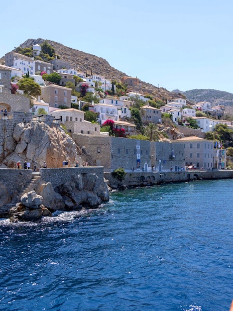 Hydra Island coastline with stone buildings and clear blue sea during Athens day cruise.