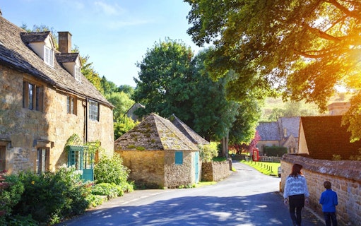 Cotswolds village street with stone cottages and people walking, ideal for a lunch tour.