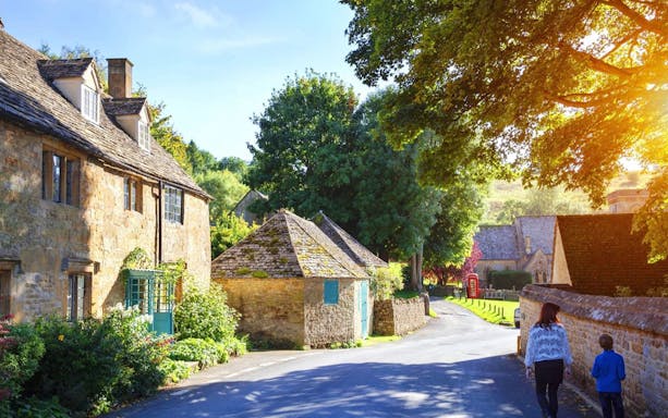 Cotswolds village street with stone cottages and people walking, ideal for a lunch tour.
