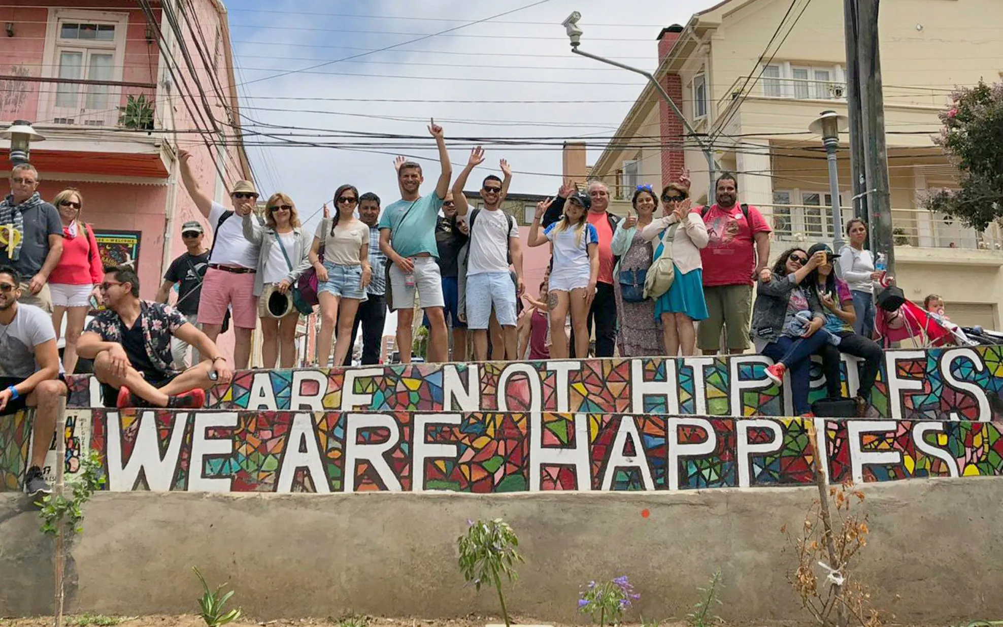 Group of people behind a colorful mural in Valparaíso, Chile, with "WE ARE NOT HIPPIES, WE ARE HAPPIES" text.