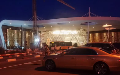 Marrakech Airport at night with parked cars and a bus in front of the terminal.