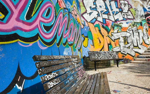 Street art mural with colorful graffiti on a wall in Lisbon, featuring benches in the foreground.