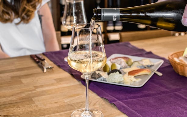 Wine being poured into a glass at a hidden wine bar with a cheese platter nearby.