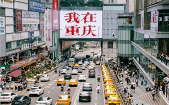 Busy street scene in Chongqing with taxis, pedestrians, and a large sign in Chinese characters.