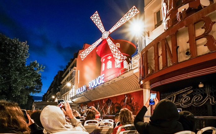 Tourists on Tootbus viewing the illuminated Moulin Rouge in Paris at night.