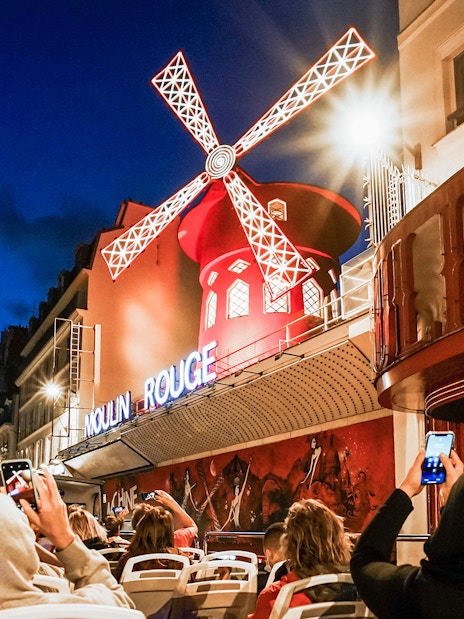 Tourists on Tootbus viewing the illuminated Moulin Rouge in Paris at night.