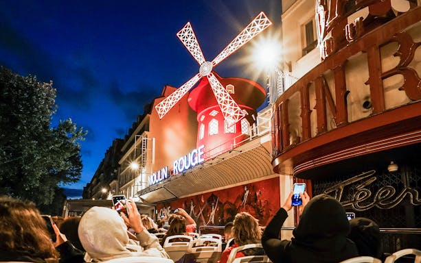 Tourists on Tootbus viewing the illuminated Moulin Rouge in Paris at night.