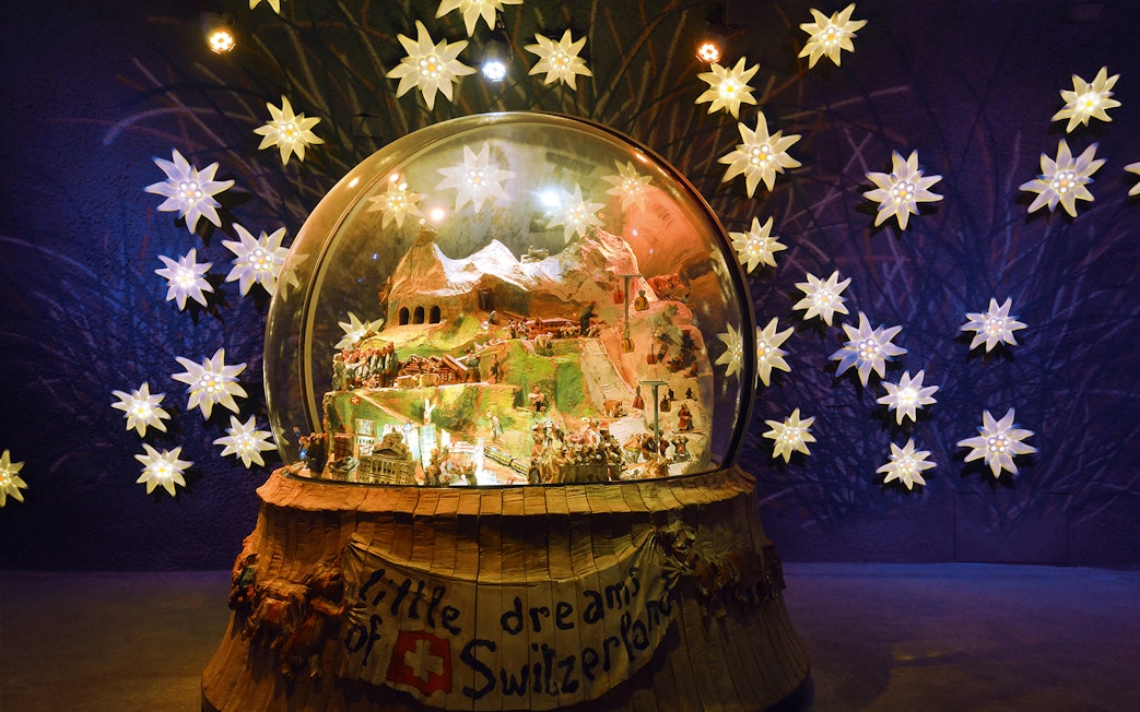 Jungfraujoch snow globe display with Swiss Alps model, surrounded by illuminated edelweiss flowers.