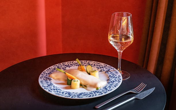 Plate of gourmet food with vegetables and sauce, paired with a glass of white wine.