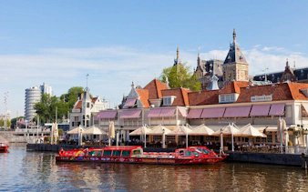 Hop-On Hop-Off boat on Amsterdam canal near historic buildings.