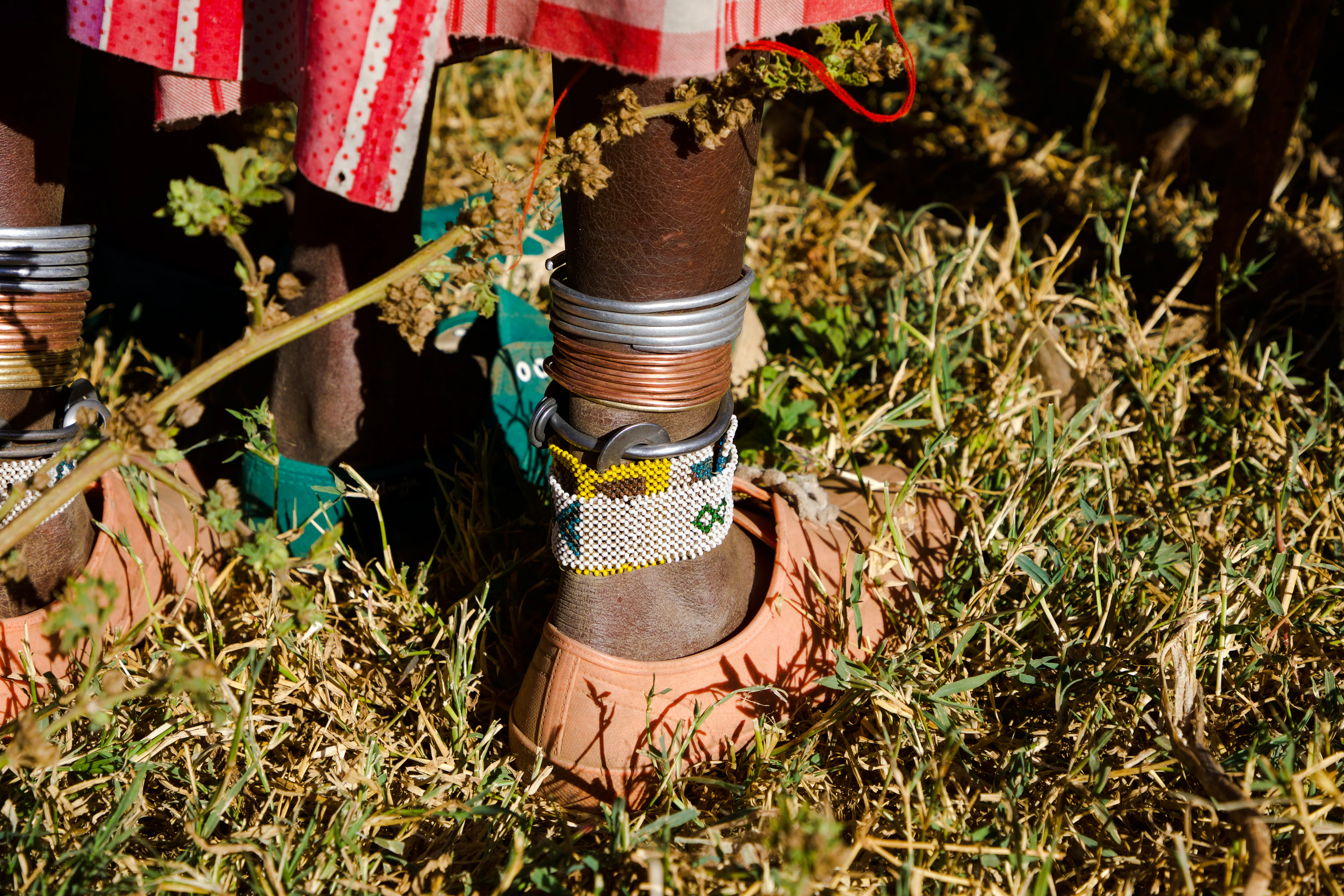Maasai ankle jewelry and sandals on grass, Zanzibar village experience.