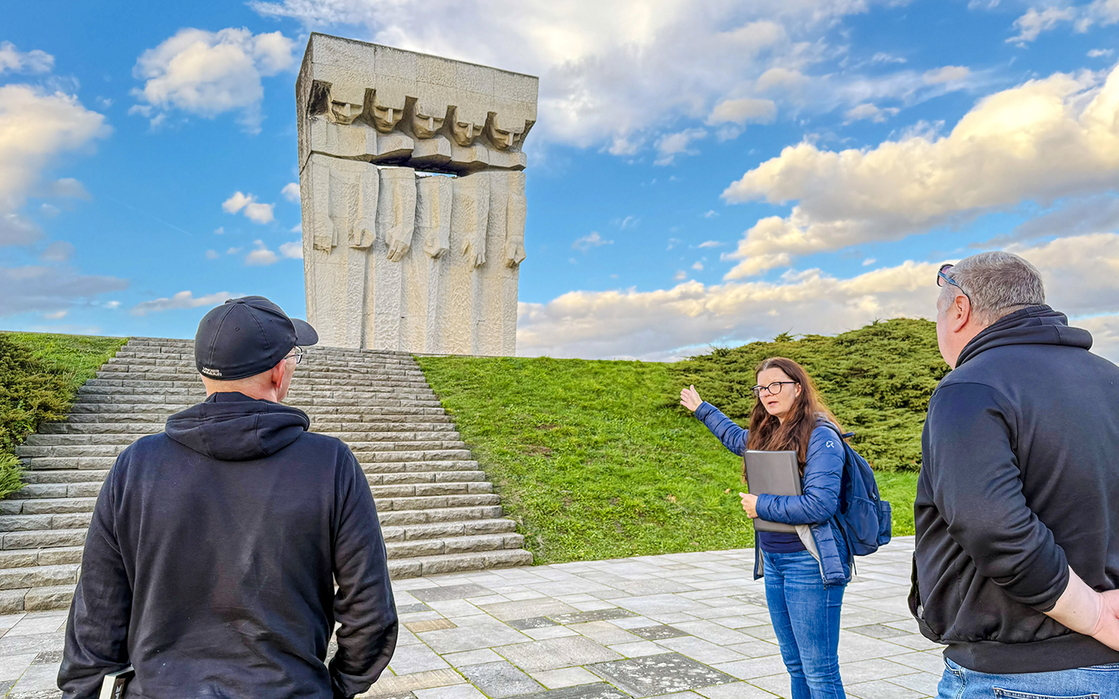 Tour guide explaining the Płaszów Concentration Camp memorial to visitors.