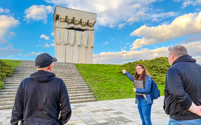 Tour guide explaining the Płaszów Concentration Camp memorial to visitors.