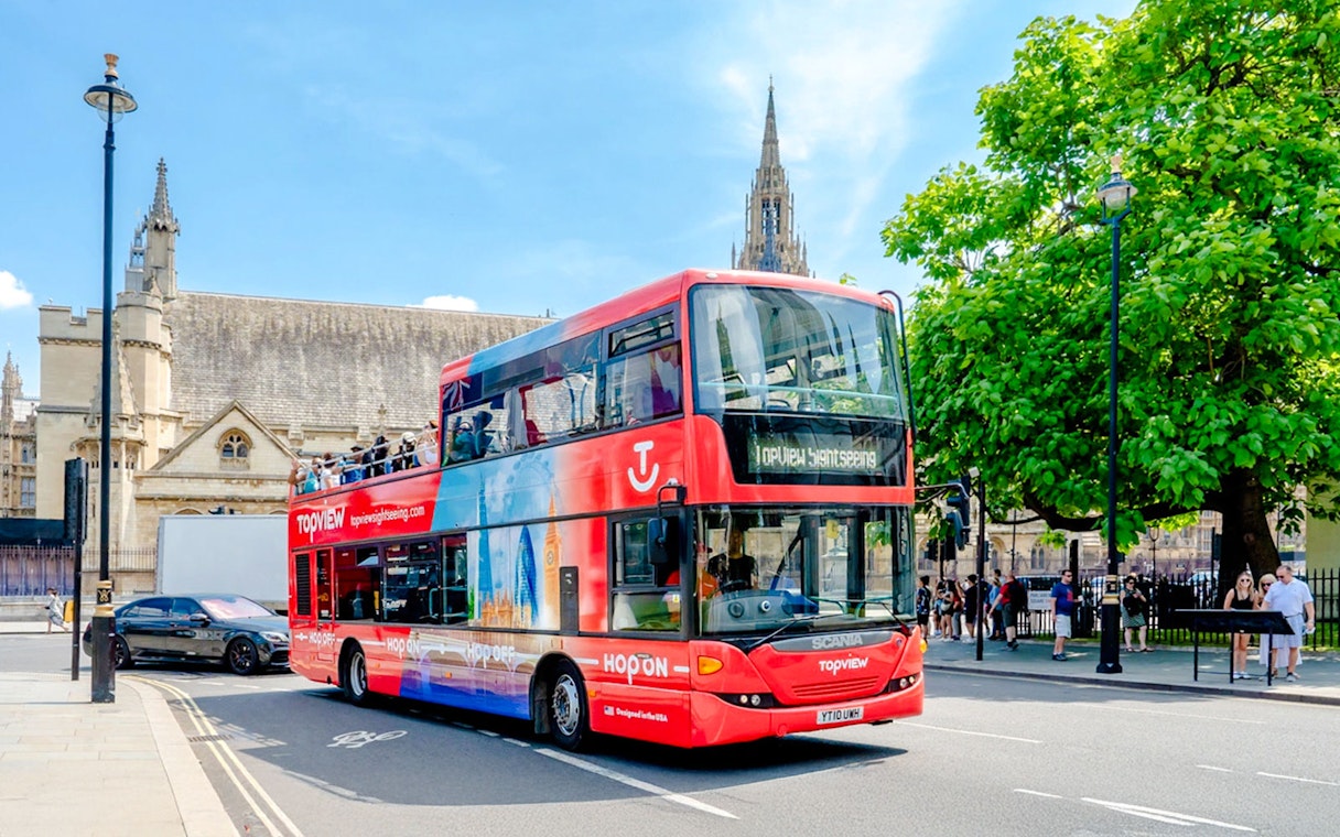 Open-top double-decker bus on London street near historic building, part of Topview HOHO tour.