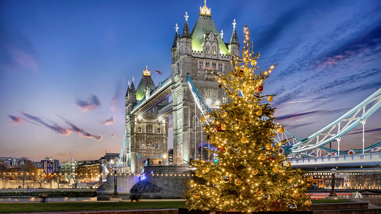 Tower Bridge in London illuminated at night with a decorated Christmas tree in the foreground.