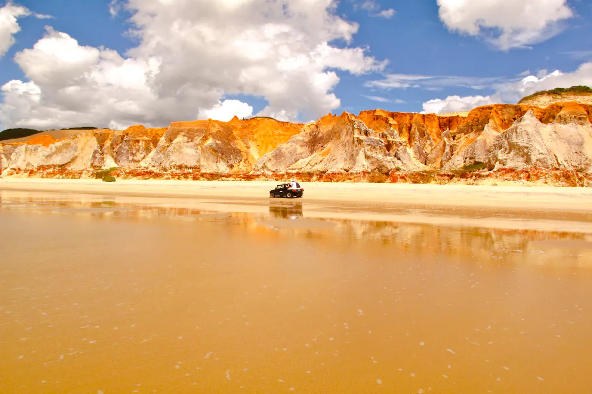 Colorful cliffs and a vehicle on the beach at Canoa Quebrada, East Coast, Brazil.