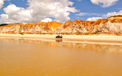 Colorful cliffs and a vehicle on the beach at Canoa Quebrada, East Coast, Brazil.