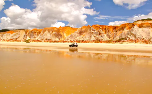Colorful cliffs and a vehicle on the beach at Canoa Quebrada, East Coast, Brazil.