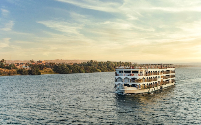 Cruise boat sailing on the Nile River with lush banks in the background.
