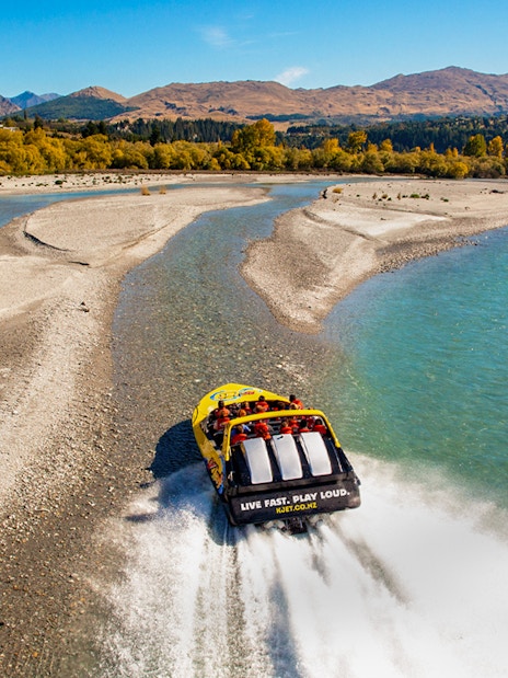 Jet boat speeding on Kawarau River with scenic mountain backdrop.
