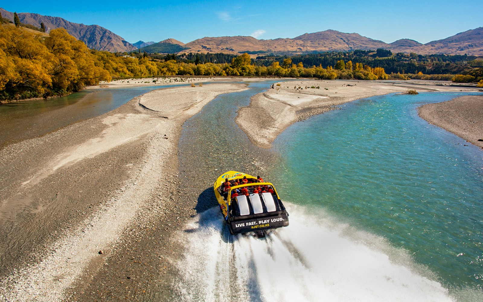 Jet boat speeding on Kawarau River with scenic mountain backdrop.