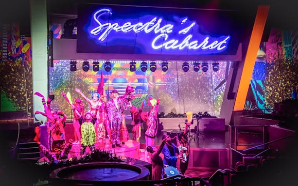 Performers on stage at Spectra's Cabaret show with vibrant costumes and neon lights.