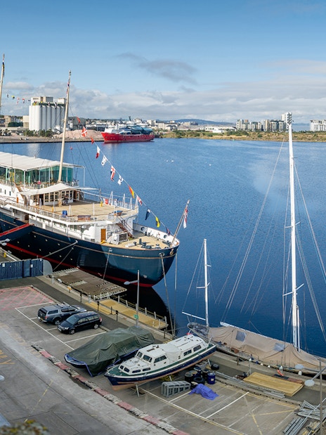 Royal Yacht Britannia docked in Edinburgh, Scotland, with cityscape in the background.