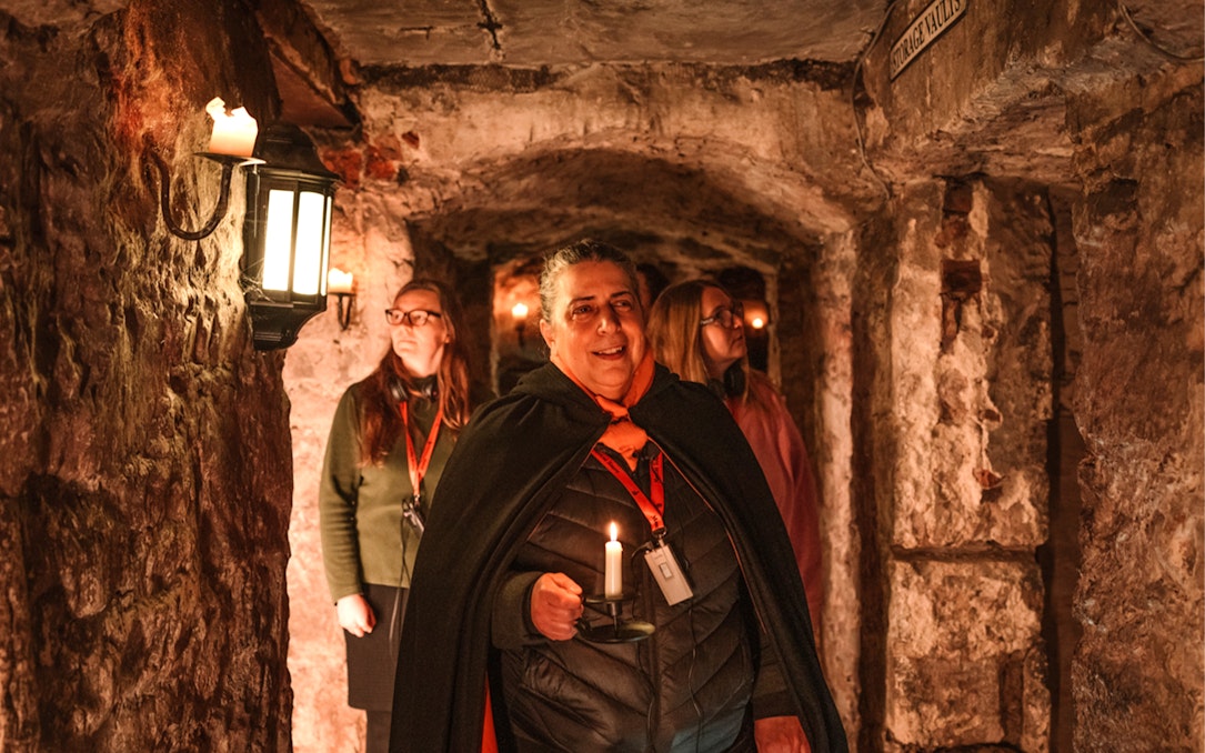 Tour guide leading a daytime underground ghost tour with visitors in a dimly lit stone vault.