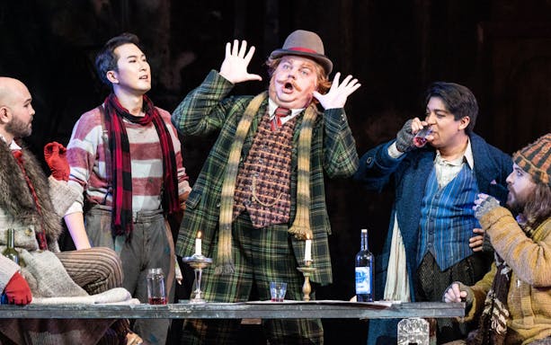 Opera performers in a lively scene from La Bohème, with expressive gestures and period costumes.