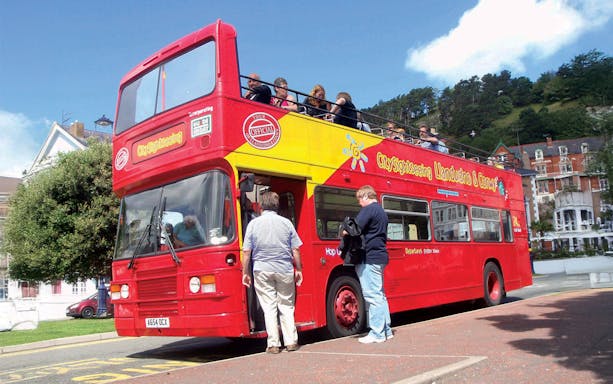 Open-top sightseeing bus in Llandudno, Wales, with tourists boarding and enjoying views.