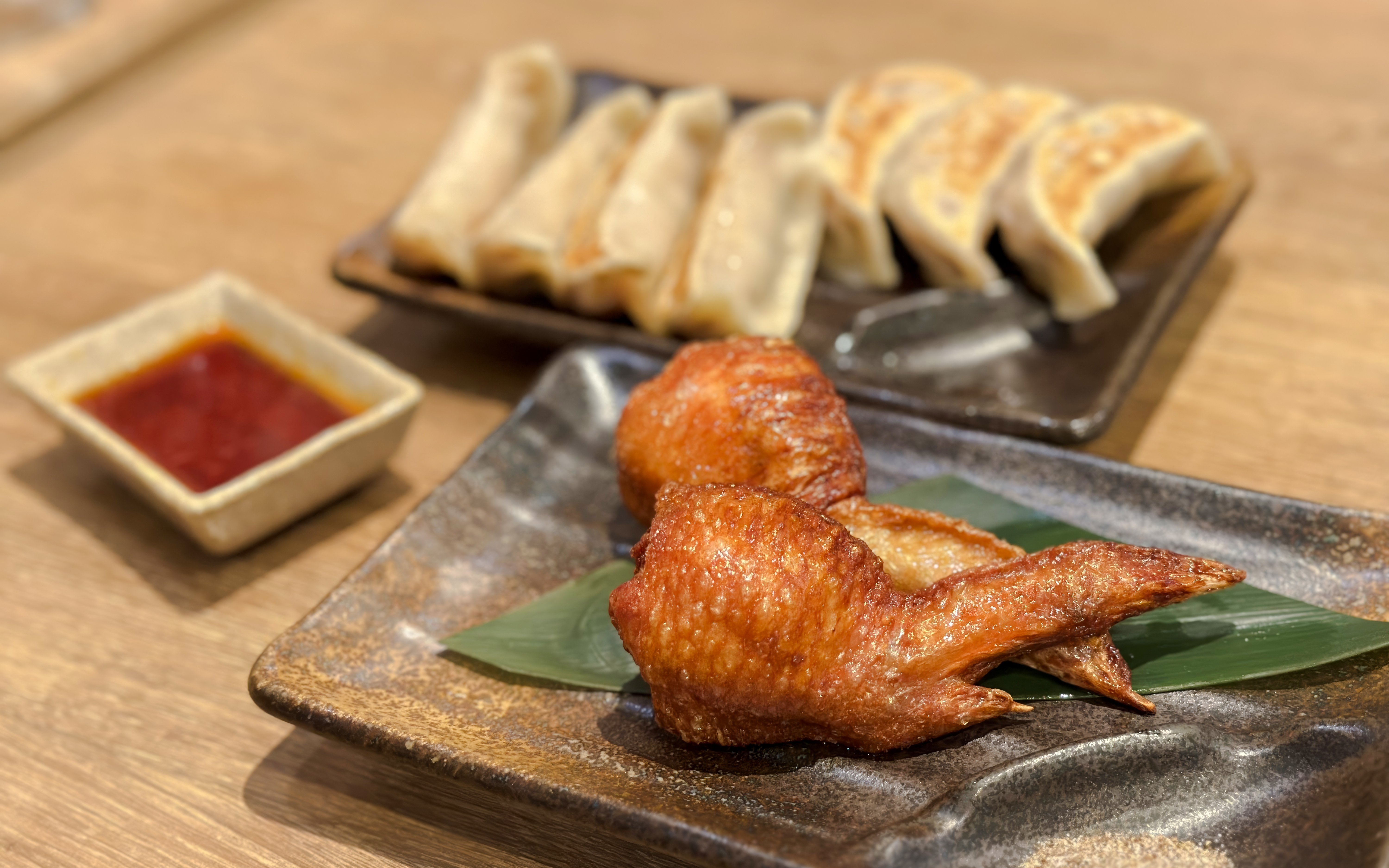 Chicken wings and gyoza on plates with dipping sauce.