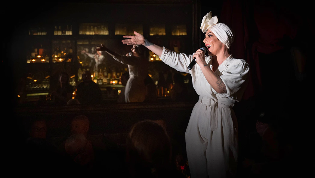 Performer singing at Miss Behaves: Maverick's Variety Show in a dimly lit venue.