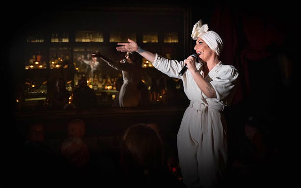 Performer singing at Miss Behaves: Maverick's Variety Show in a dimly lit venue.