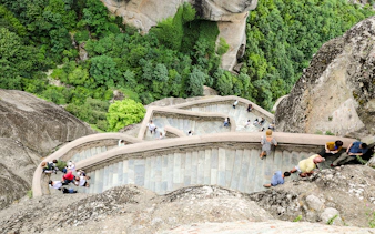 Tourists walking on the stone stairs of the Monastery of Varlaam, surrounded by lush greenery.