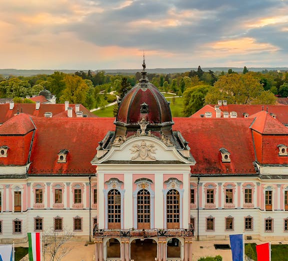 Baroque palace facade with red roof in Godollo, near Budapest, surrounded by gardens.