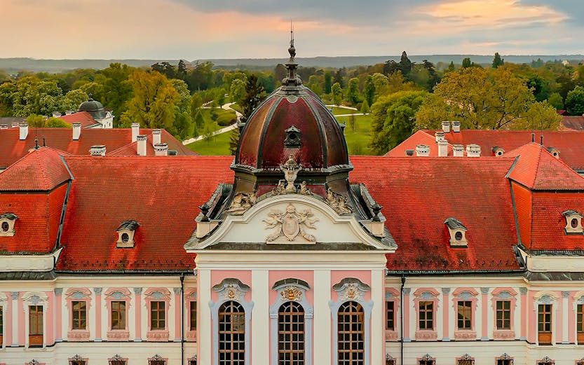Baroque palace facade with red roof in Godollo, near Budapest, surrounded by gardens.