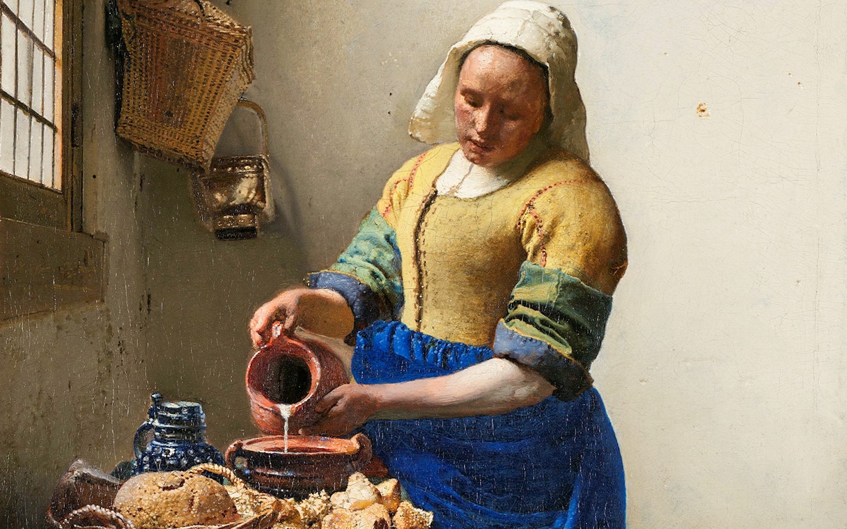 Woman pouring milk in Vermeer's "The Milkmaid," c. 1660, with bread and pottery on the table.