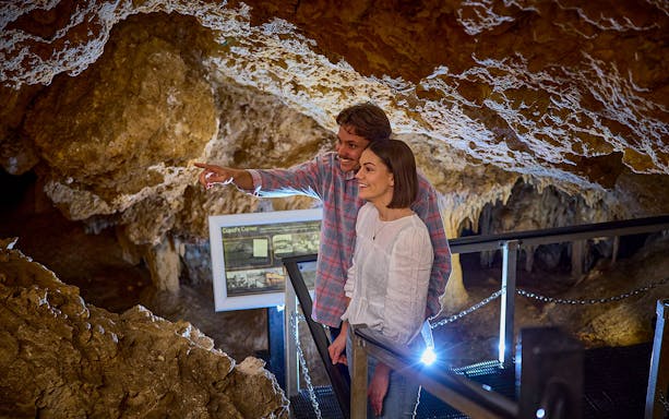Couple exploring Ngilgi Cave on a semi-guided tour, observing rock formations.