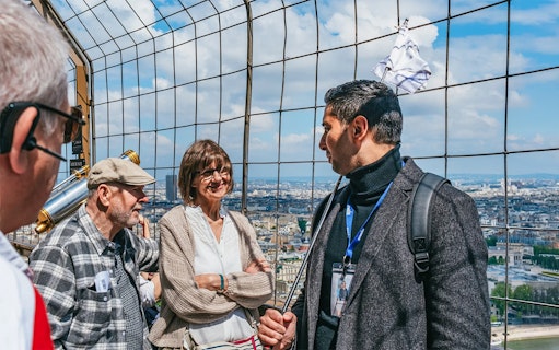 Tourists with guide on Eiffel Tower observation deck overlooking Paris.