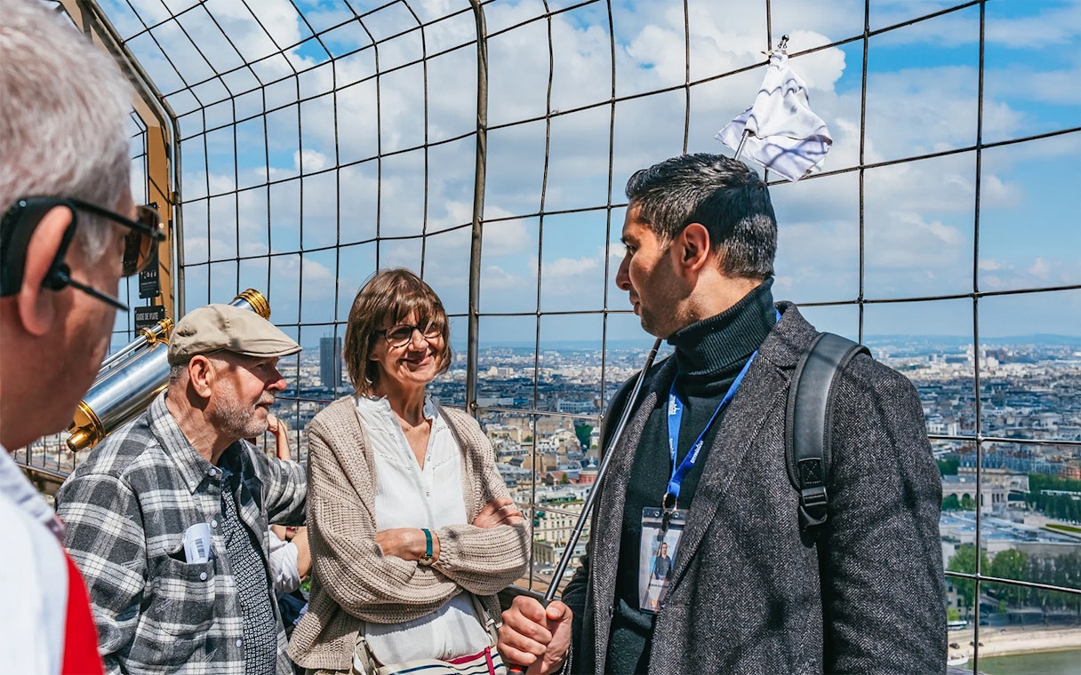 Tourists with guide on Eiffel Tower observation deck overlooking Paris.