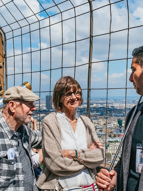Tourists with guide on Eiffel Tower observation deck overlooking Paris.