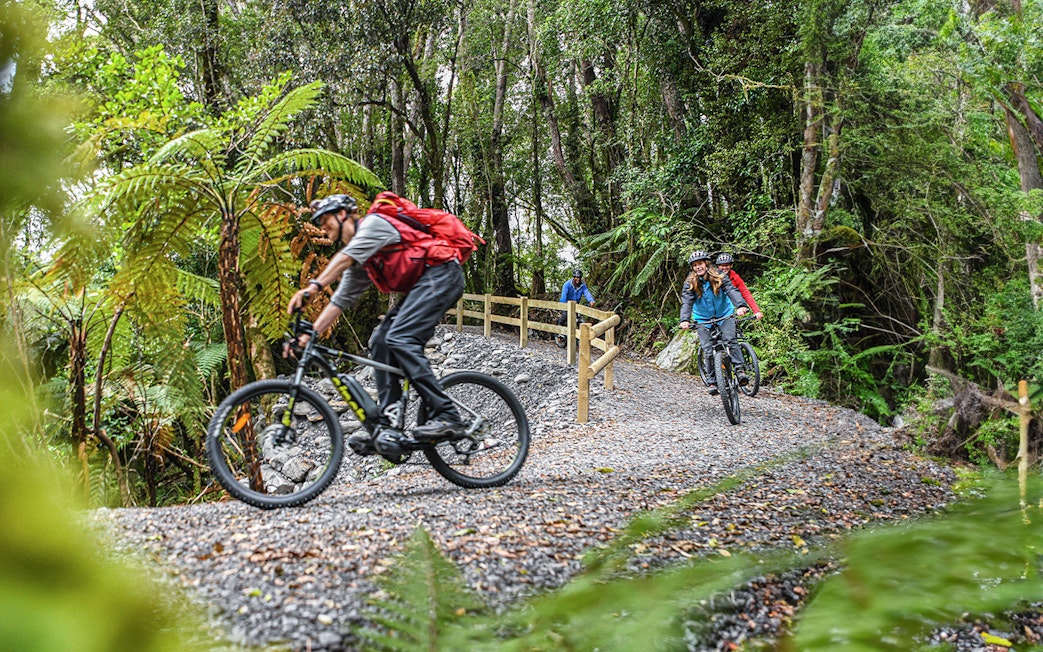 Cyclists on a guided e-bike tour through Fox Glacier Valley forest trail.