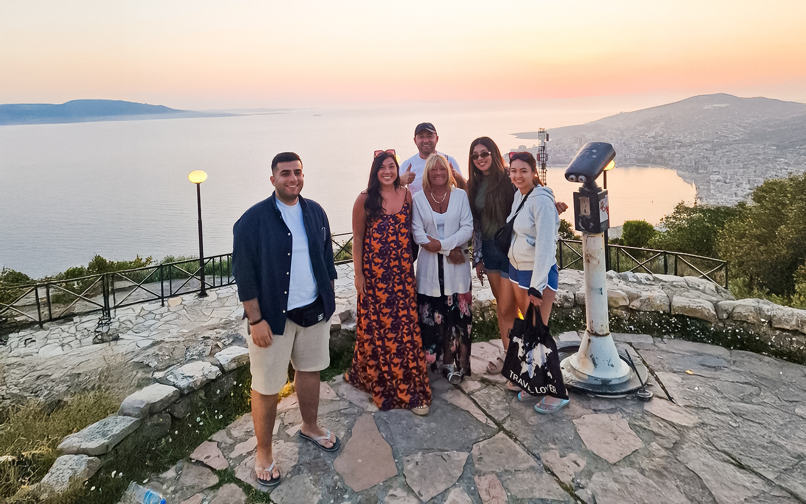 Guests enjoying sunset at Lekursi Castle with a view of the sea and distant hills.