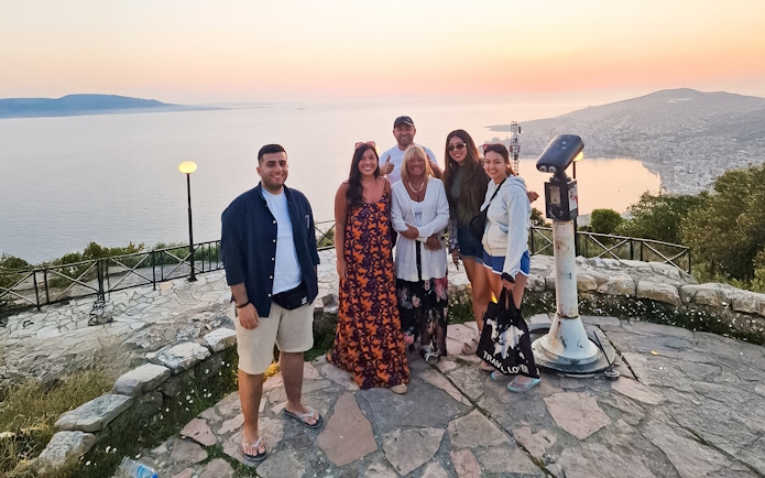 Guests enjoying sunset at Lekursi Castle with a view of the sea and distant hills.