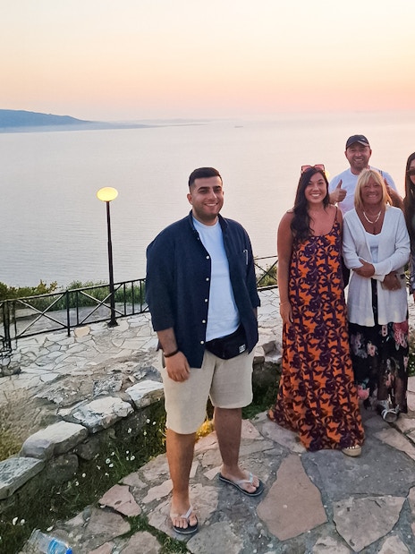 Guests enjoying sunset at Lekursi Castle with a view of the sea and distant hills.